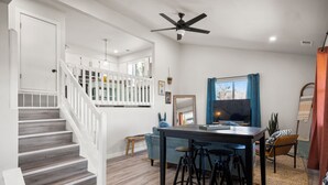 A modern living room with a staircase, a dining area with stools, and a large window with curtains. - The Heritage Hideaway Views Games & More (Leander)