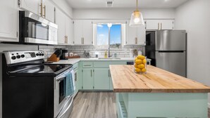 A modern kitchen with white cabinets, a black stove, a stainless steel refrigerator, and a wooden island with lemons. - The Heritage Hideaway Views Games & More (Leander)
