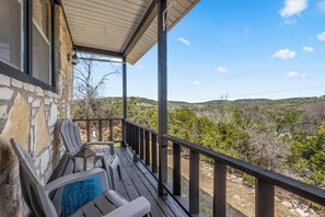 Eine Holzterrasse mit Sitzgelegenheit, eine Steinmauer und Blick auf eine hügelige Landschaft.