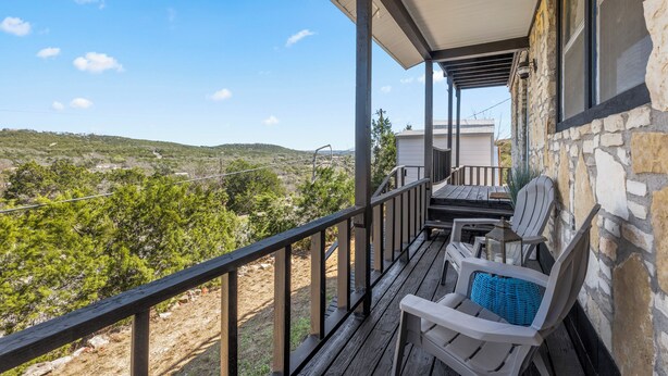 A balcony with a view of a hilly landscape, a stone wall, and two Adirondack chairs. - The Heritage Hideaway Views Games & More (Leander)