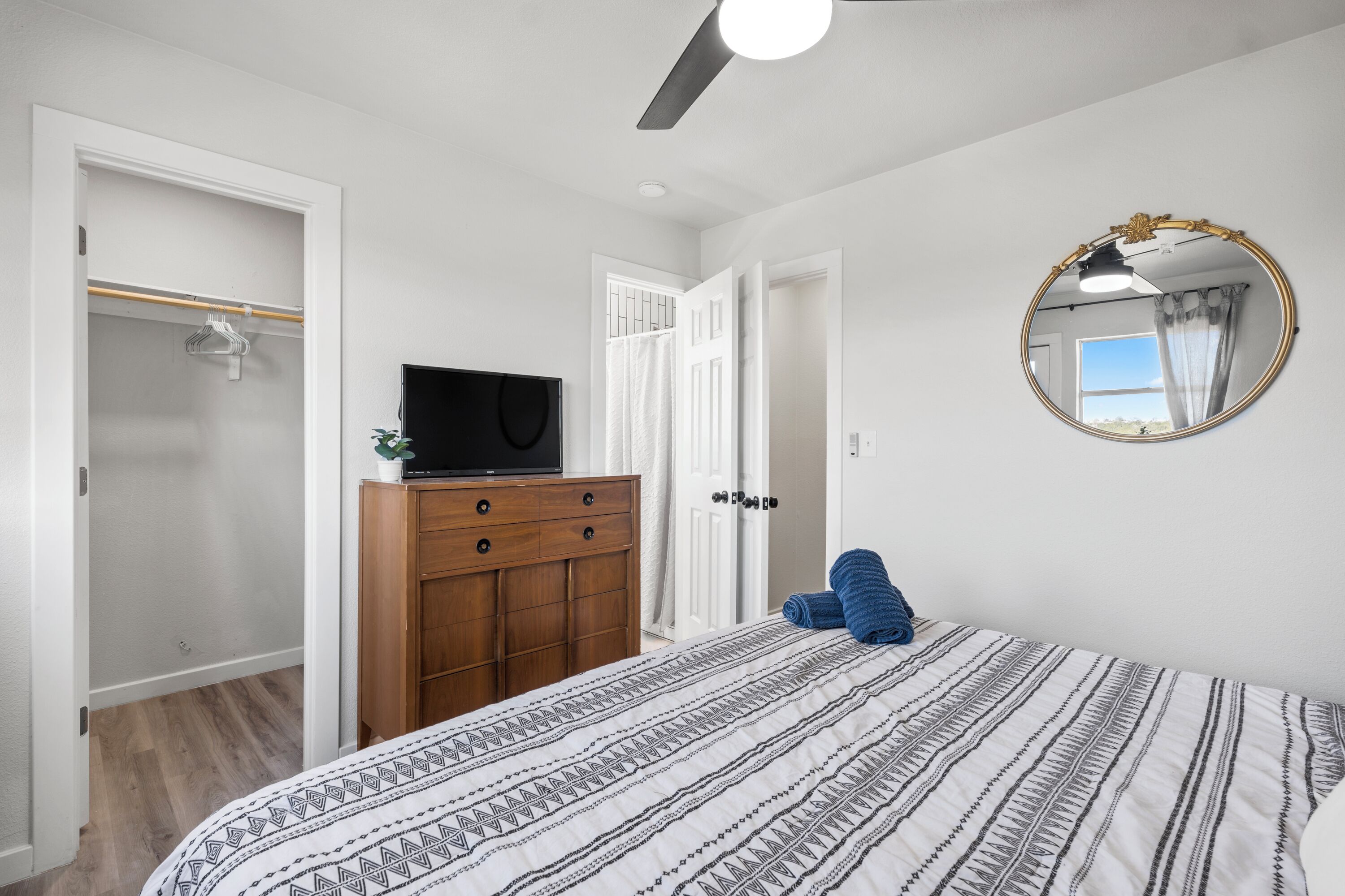 Une chambre à coucher avec un lit, une commode en bois, un téléviseur et un miroir au mur.