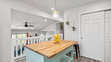 Una cocina con una isla de madera, paredes blancas y un ventilador de techo.