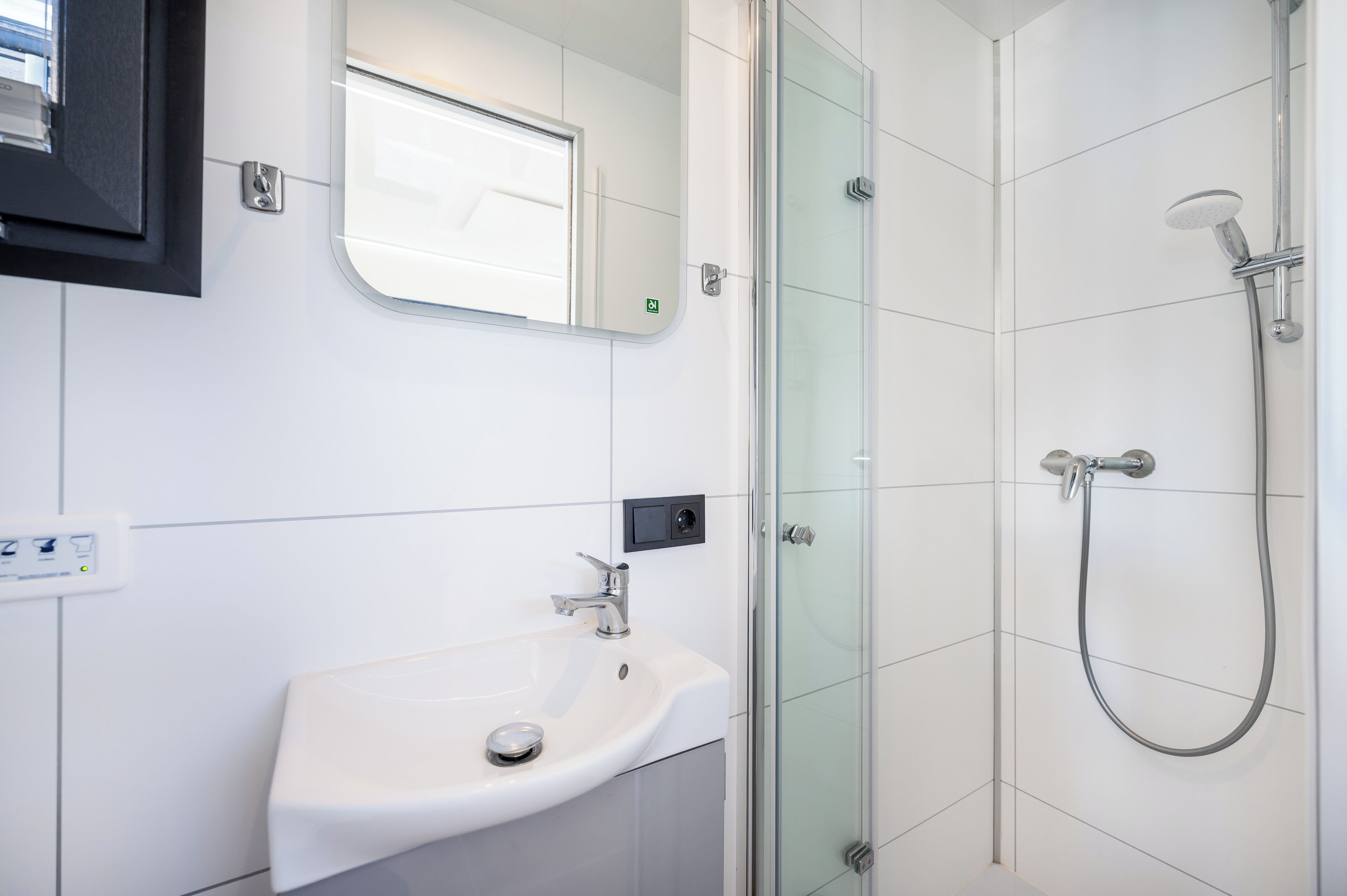 Ein modernes Badezimmer mit einem weißen Waschbecken, einer Duschkabine aus Glas und einem Spiegel über dem Waschbecken.