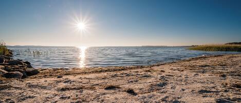 A beach with a clear sky and the sun reflecting on the water.