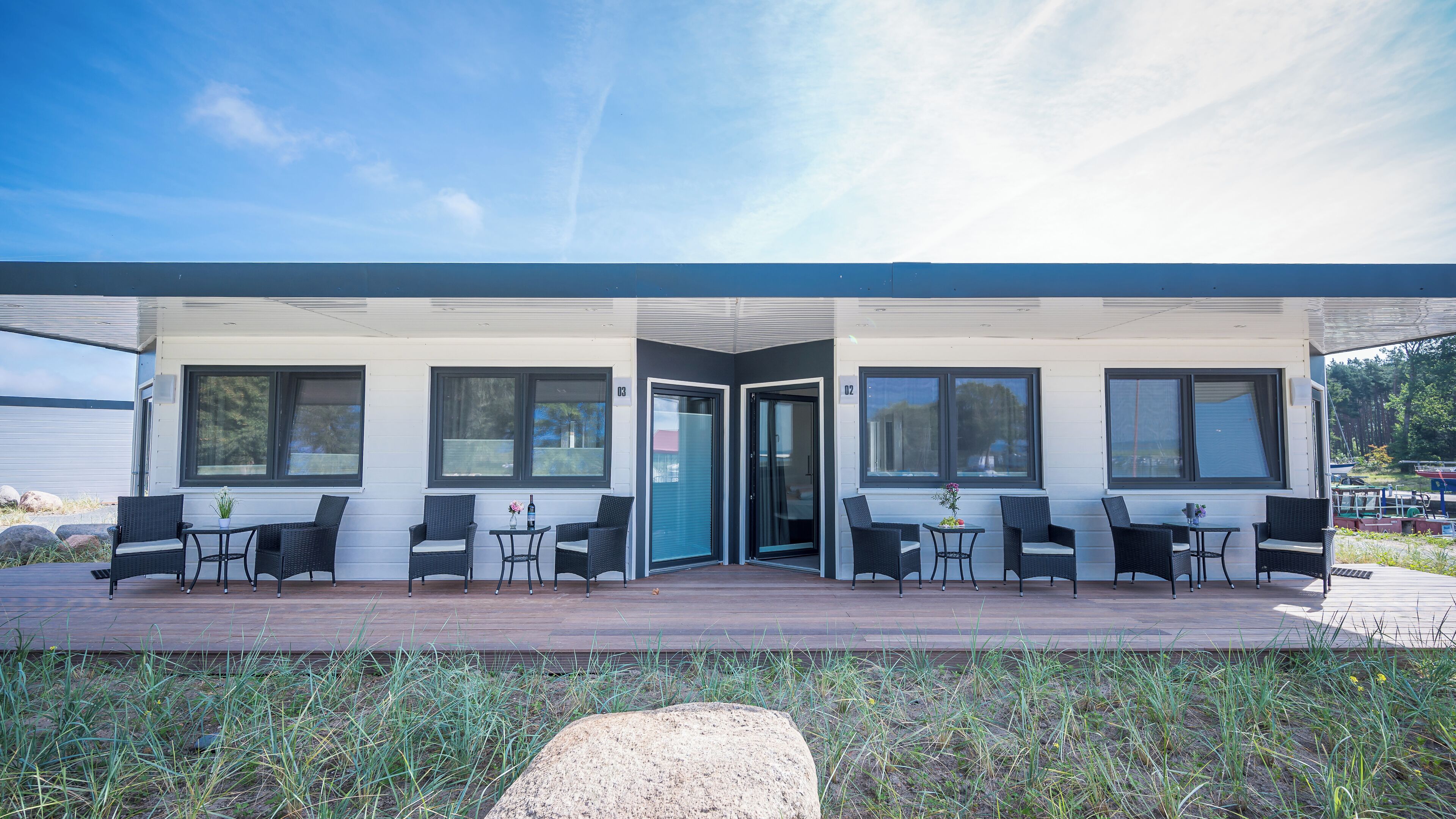 A modern building with a covered patio area featuring outdoor seating and a small table with a vase of flowers.