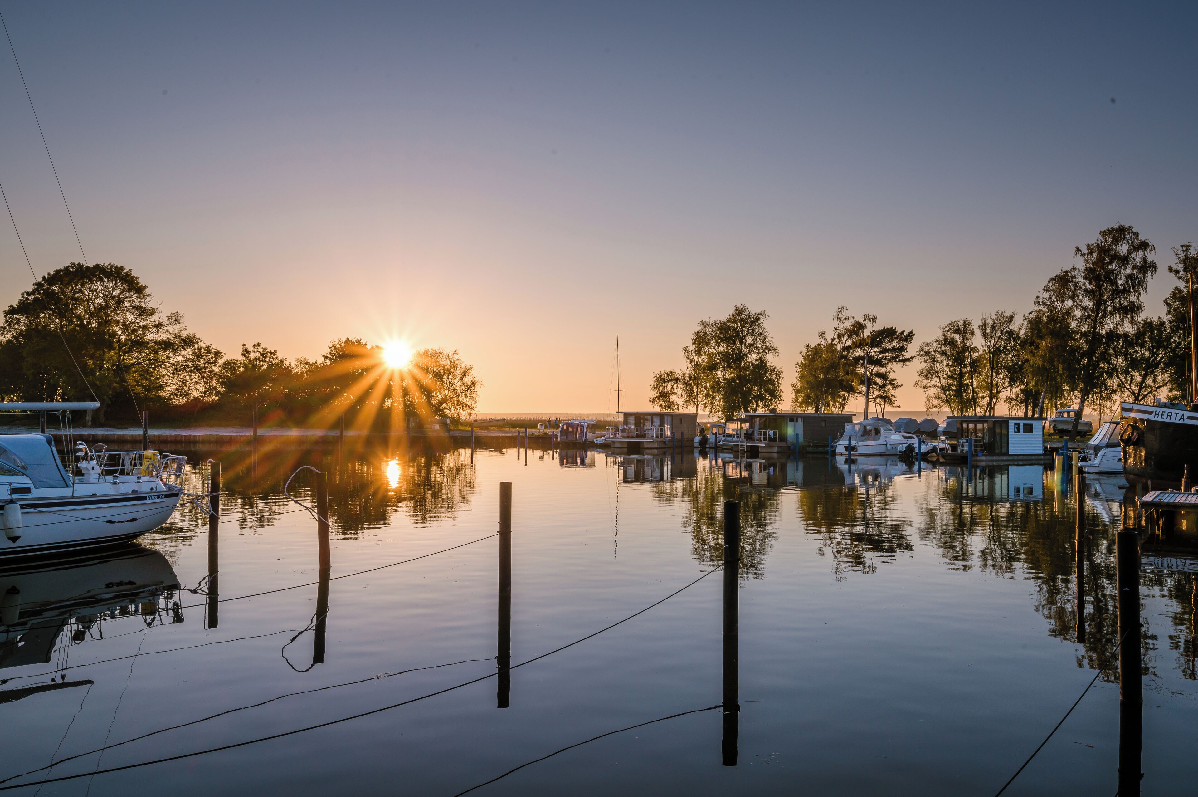 Un port de plaisance avec des bateaux amarrés, une eau calme et un coucher de soleil en arrière-plan.