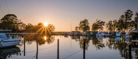 Un port de plaisance avec des bateaux amarrés, une eau calme et un coucher de soleil en arrière-plan.