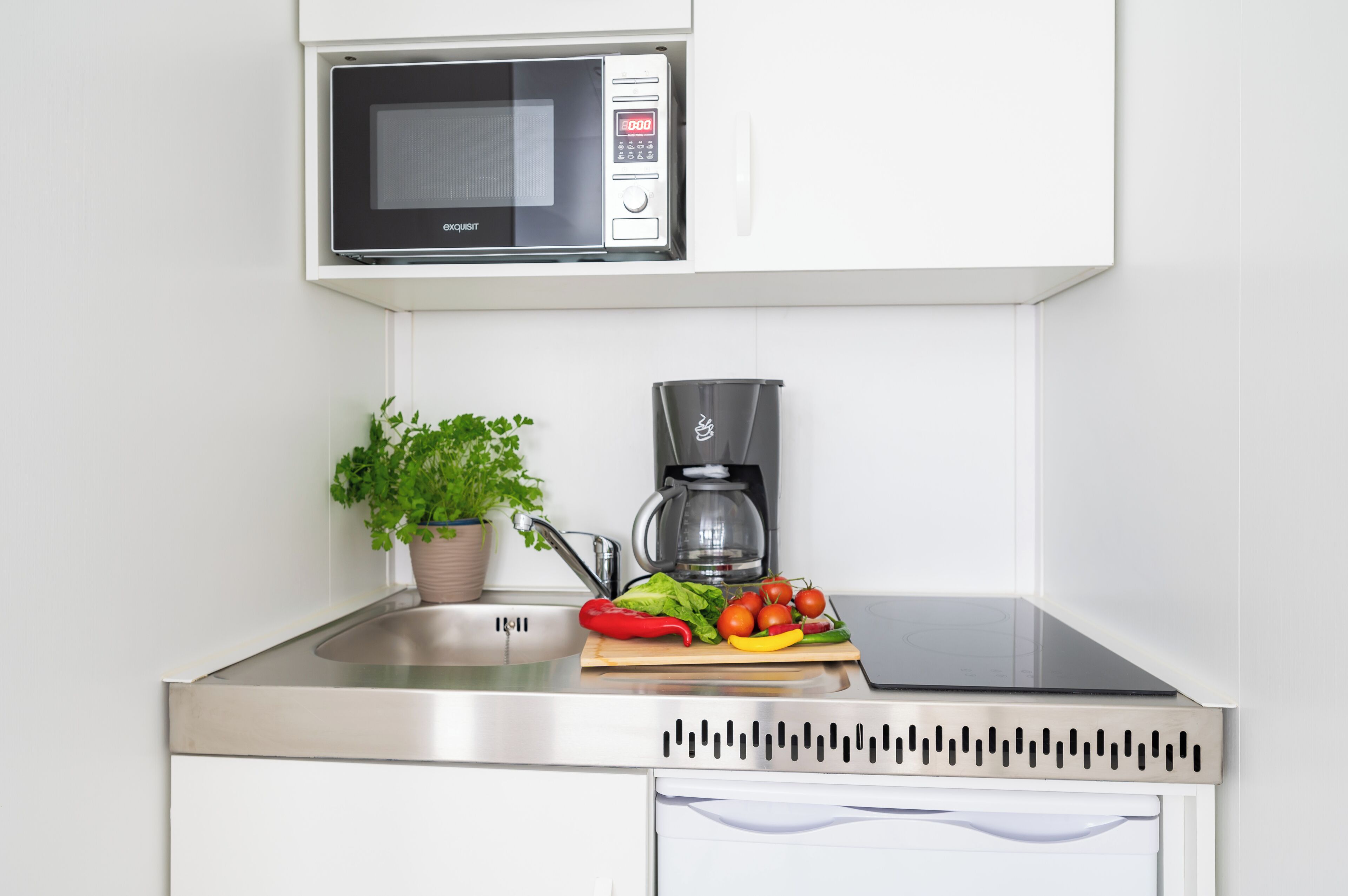 Una cocina con microondas, cafetera y verduras frescas en la encimera.