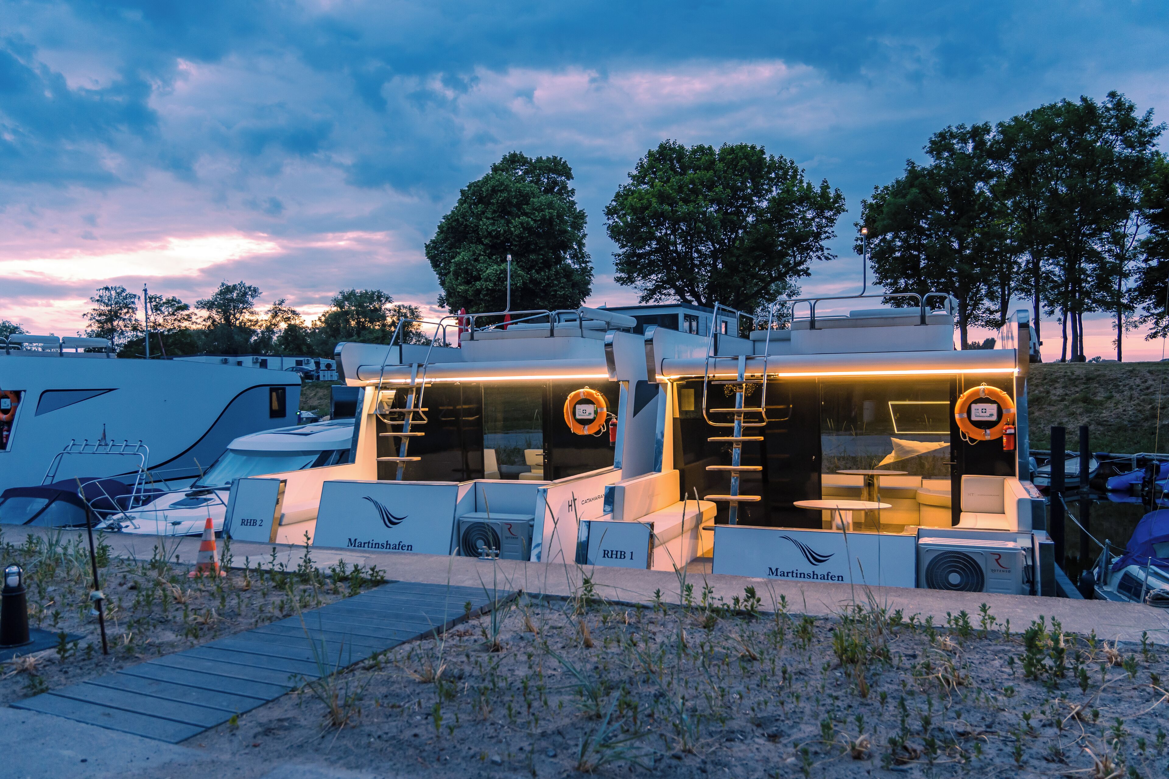 A modern RV with a kitchen area, two lifeboats, and a deck.