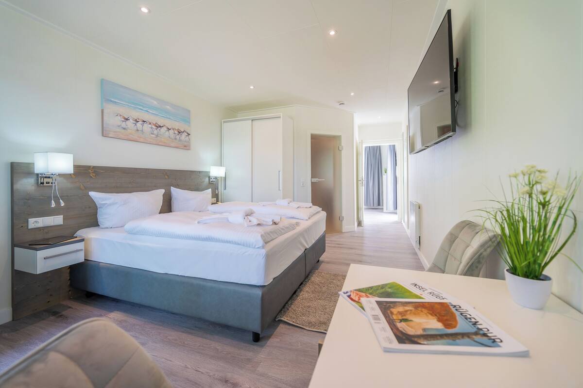 Een moderne hotelkamer met een bed, nachtkastjes, een televisie en uitzicht op de gang.