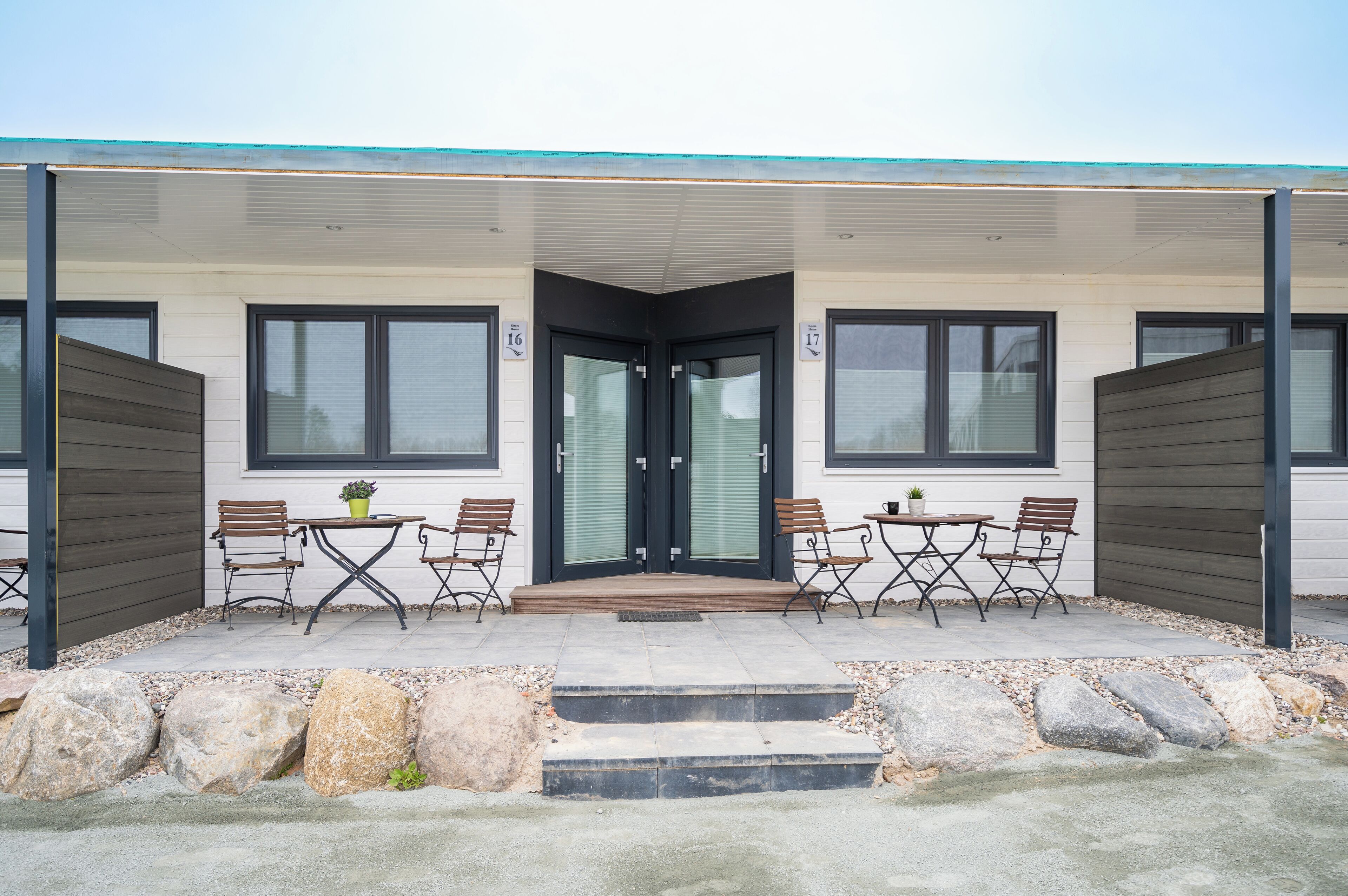 A modern building with a covered patio area featuring outdoor seating and a staircase leading to the entrance.