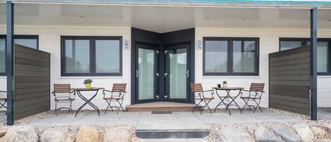 A modern building with a covered patio area featuring outdoor seating and a staircase leading to the entrance.