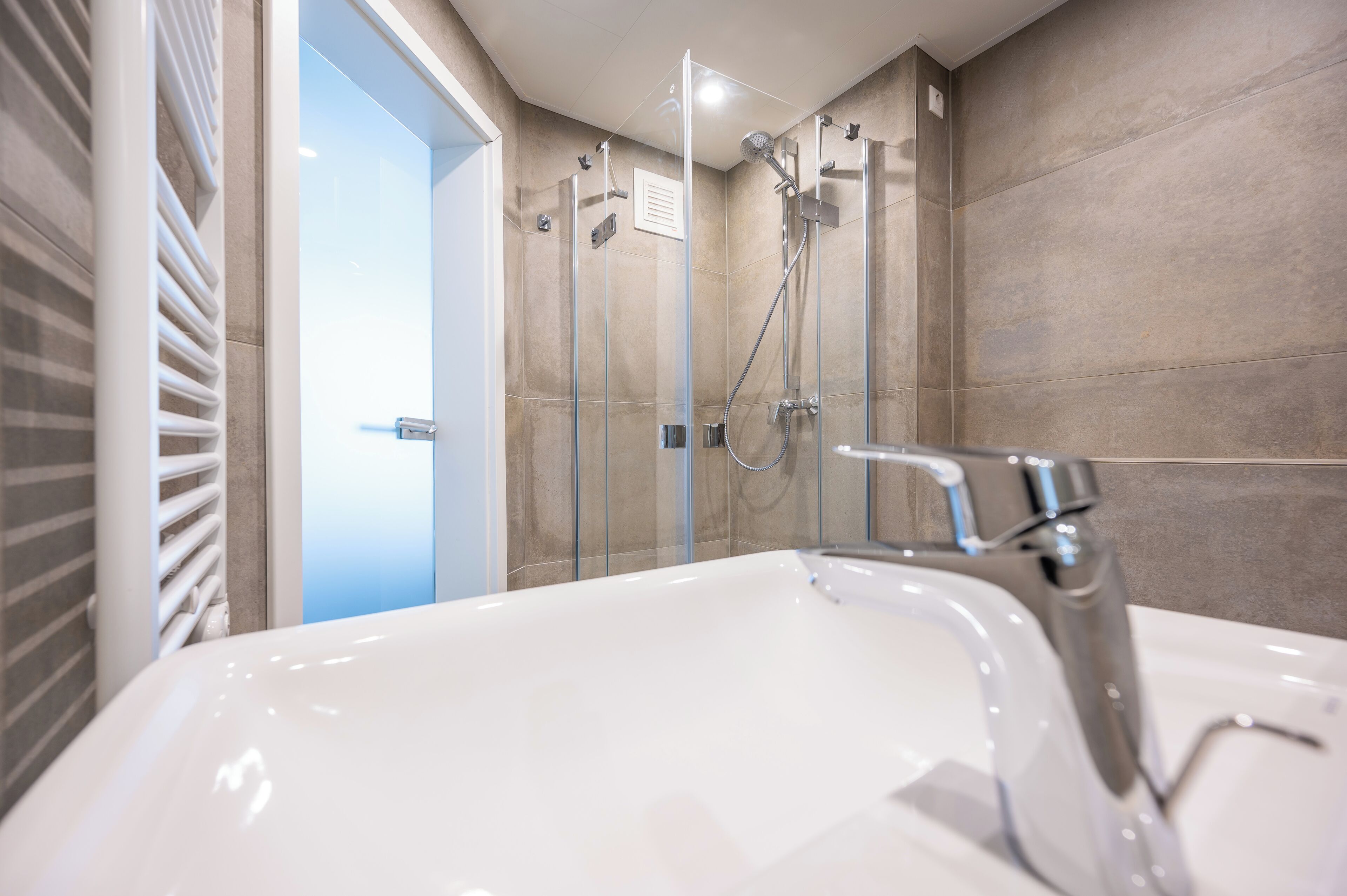 A modern bathroom with a large white sink, a glass shower enclosure, and beige tiled walls.
