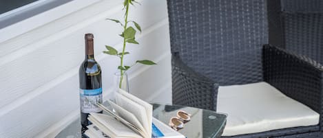 A glass table with a wine bottle, an open book, a pair of glasses, and a rose.