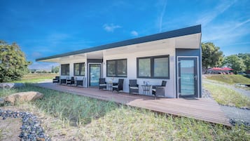 Un edificio moderno con un área de estar cubierta al aire libre, ventanas amplias y una terraza de madera.