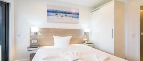 A hotel room with a large bed, a wooden headboard, a painting of birds on the wall, and a neatly made bed with towels.