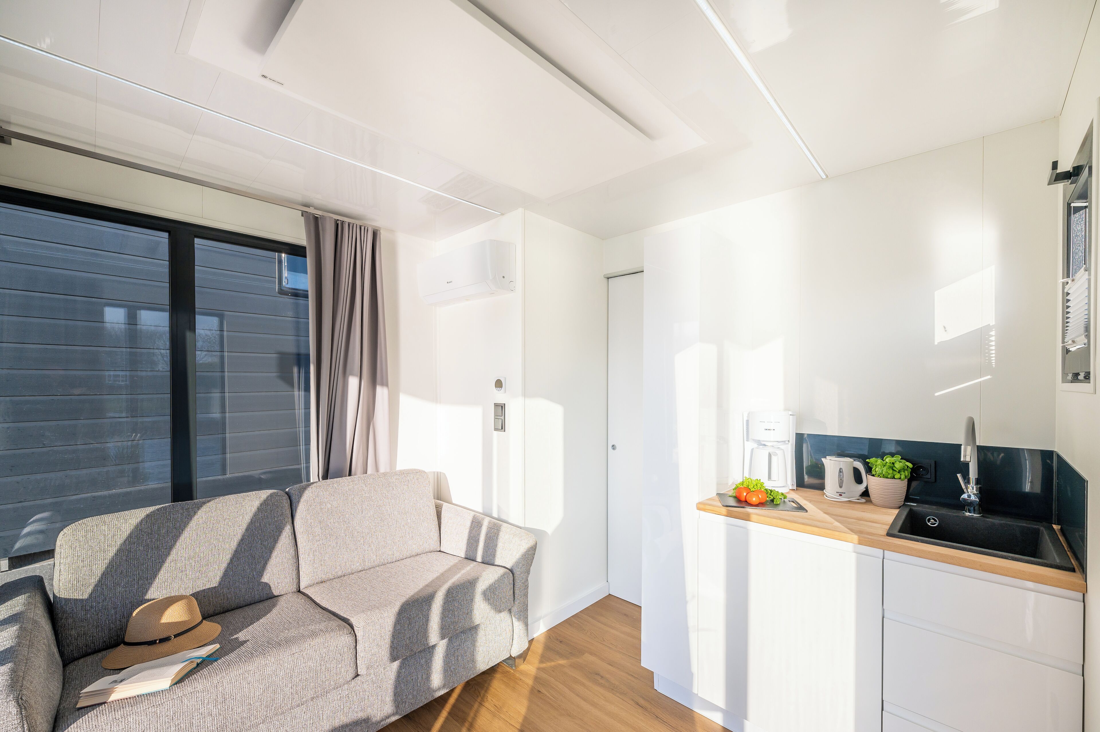 Uma sala de estar moderna com sofá e uma mesinha, cozinha com pia e bancada, e uma grande janela que proporciona luz natural.