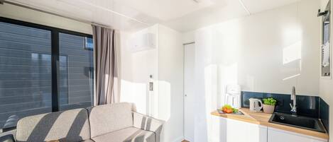 Uma sala de estar moderna com sofá e uma mesinha, cozinha com pia e bancada, e uma grande janela que proporciona luz natural.