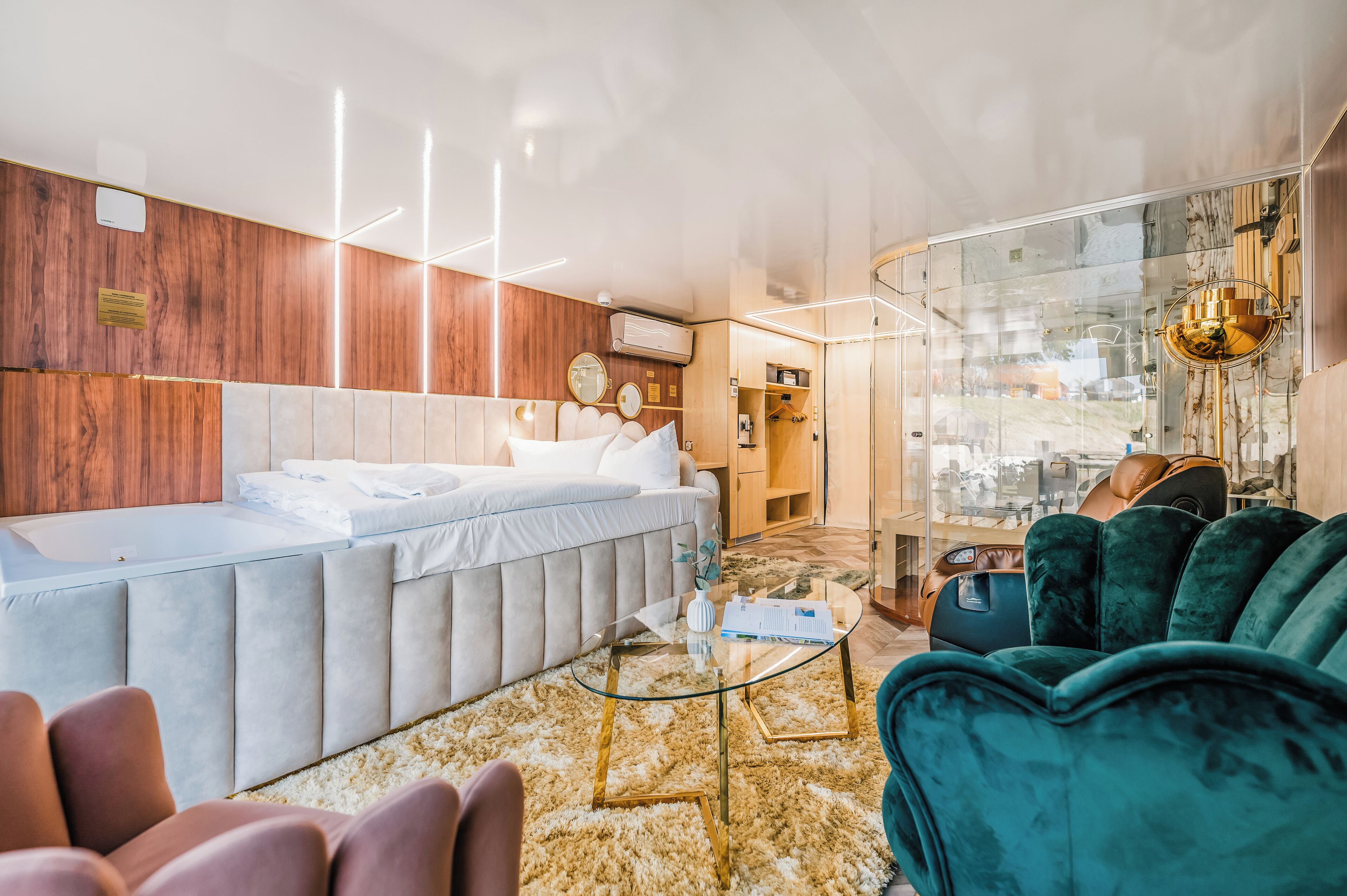 A modern hotel room with a large bed, a glass coffee table, and a seating area with a green sofa.