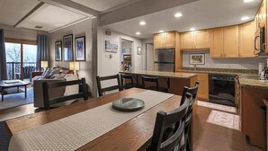 A modern kitchen with wooden cabinets, a built-in oven, and a dining area with a wooden table and chairs. - Rocky Mountain Sanctuary (Steamboat Springs)