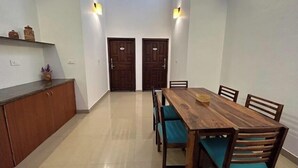 A dining area with a wooden table and chairs, a kitchen counter, and two doors. - Villa Mercara (Madikeri)