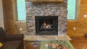 A stone fireplace with a fire, a framed picture above it, and a shelf with books.