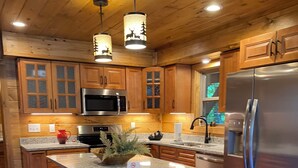 A kitchen with wooden cabinets, a stainless steel refrigerator, a granite countertop, and a bar stool.