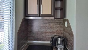 A compact kitchen with dark wooden cabinets, a built-in microwave, and a coffee maker on the counter.