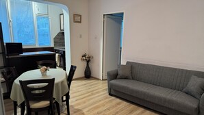 A living room with a grey sofa, a dining table with chairs, a vase with flowers, and a kitchen area with a microwave.