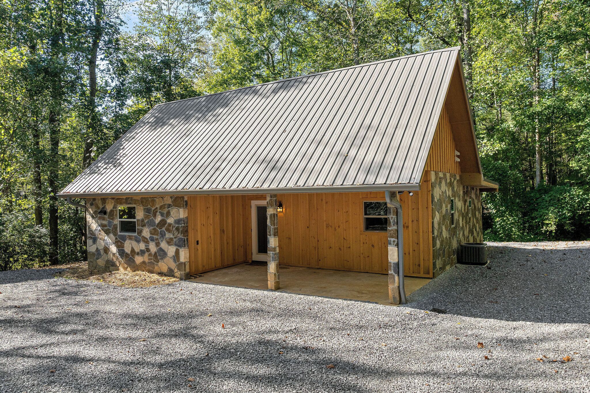 A rustic cabin with a sloped metal roof, stone and wooden walls, and a gravel driveway.