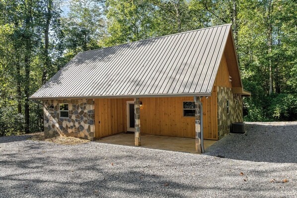 A rustic cabin with a sloped metal roof, stone and wooden walls, and a gravel driveway.