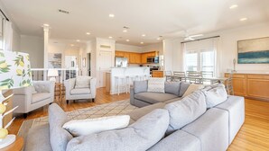 A modern living room with a grey sectional sofa, a small white table, and a kitchen in the background. - 30A Beach House ~ Gulf Views ~ Gated Beach Access (Seacrest Beach)