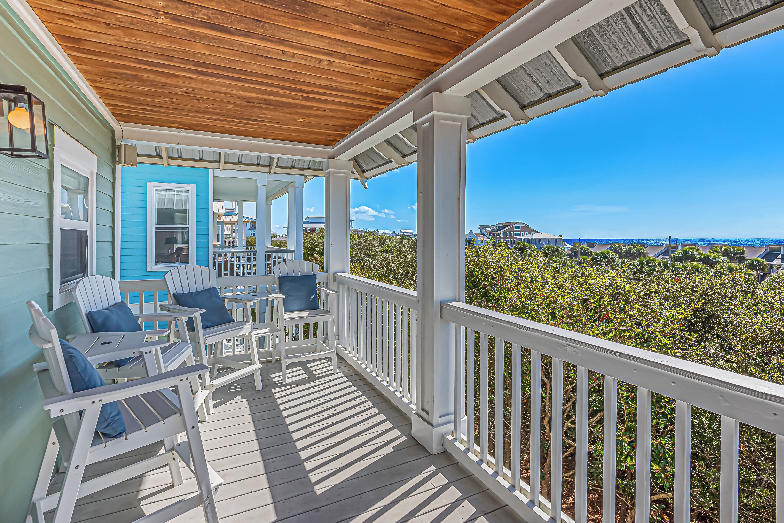 A covered porch with white railings and Adirondack chairs, overlooking a coastal landscape.