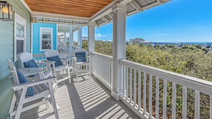 A covered porch with white railings and Adirondack chairs, overlooking a coastal landscape. - 30A Beach House ~ Gulf Views ~ Gated Beach Access (Seacrest Beach)