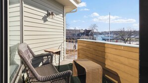 A balcony with wicker furniture, a view of a building across the street, and a stop sign in the background. - 200 Pointes North | Water View | Downtown Charlevoix | Indoor/Outdoor Pool (Charlevoix)