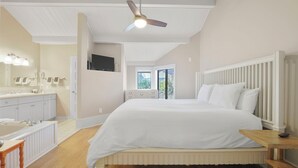 A bedroom with a large bed, a ceiling fan, a window, and a bathroom with a bathtub and sink. - 200 Pointes North | Water View | Downtown Charlevoix | Indoor/Outdoor Pool (Charlevoix)
