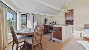 A modern kitchen with a central island, a dining area with a table and chairs, and a view through large windows. - 200 Pointes North | Water View | Downtown Charlevoix | Indoor/Outdoor Pool (Charlevoix)