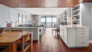 A modern kitchen with a wooden dining table, white cabinetry, and a view to the outside. - HPN-Stunning 2 Bedroom Direct Ocean Front Condo (Ocean City)