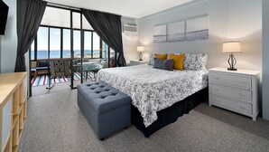 A bedroom with a large bed, a desk, a chair, and a view of the sea. - HPN-Stunning 2 Bedroom Direct Ocean Front Condo (Ocean City)