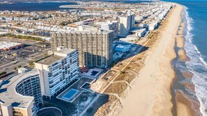 A coastal cityscape with a beachfront hotel featuring multiple floors, a parking lot, and a swimming pool. - HPN-Stunning 2 Bedroom Direct Ocean Front Condo (Ocean City)