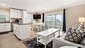Une cuisine moderne avec des meubles blancs, un coin repas comprenant une table et des chaises, et un balcon offrant une vue sur les immeubles.