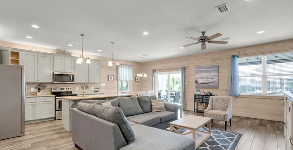 A modern kitchen with grey cabinets, a microwave, and a dining area with a grey sofa and a patterned armchair.