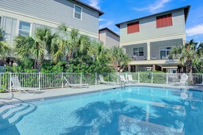 A swimming pool with lounge chairs, surrounded by palm trees and a white fence.