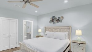 Een slaapkamer met een bed, twee nachtkastjes met lampen, een plafondventilator, een witte deur en een decoratief wandobject.