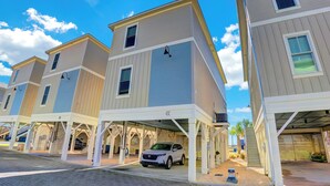 A row of modern, multi-story buildings with covered parking areas and a white SUV parked under one of the structures. - West Side Cottages CC by Liquid Life (Gulf Shores)