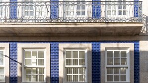 Fachada de edificio con tres ventanas y un balcón con barandilla de metal ornamental.