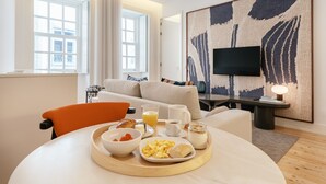Ett modernt hotellrum med en matplats som inkluderar frukostalternativ, en soffa, en TV och en stor, abstrakt målning.