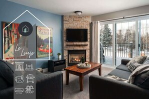 Una sala de estar con chimenea, un televisor de pantalla plana y un ventanal con vistas a árboles.