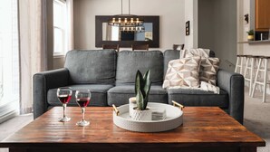 Un salon avec un canapé gris, une table basse en bois et deux verres à vin.