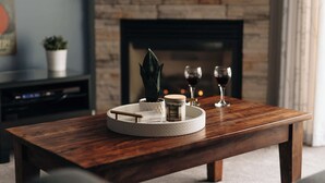 Une table basse en bois avec un plateau, une plante en pot, une bougie et deux verres à vin.